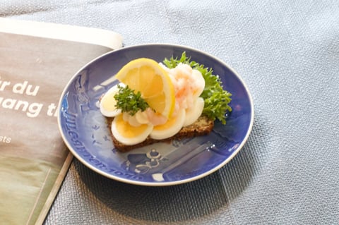 Open-faced sandwich with sliced eggs and smoked salmon on toasted bread with greens, served on a blue plate