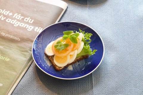 Open-faced sandwich with sliced eggs, tomato, and greens on toast in a blue bowl