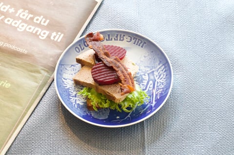 Blue and white decorative plate with sliced smoked fish, beets, and lettuce served on a textured linen surface next to a Swedish cookbook