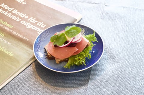Small plate with sliced ham, fresh lettuce, and garnish on blue dish next to menu card