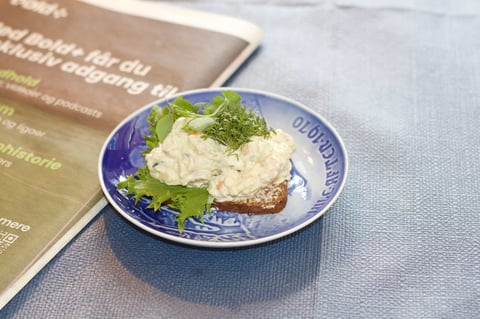 Plate of egg salad sandwich on rye bread garnished with fresh dill, next to a menu