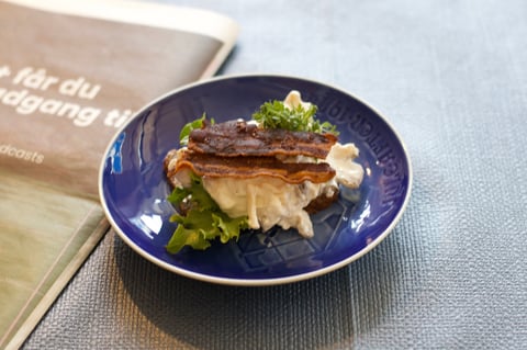 Gourmet dish with seared protein, creamy sauce, and microgreens on a blue plate next to a menu