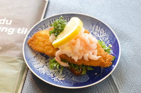Breaded fried cutlet topped with shrimp and garnished with lemon and greens on a blue plate