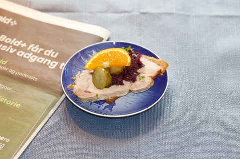 Open-faced sandwich on blue plate with smoked salmon, orange slice, capers, and beet, beside Swedish text menu