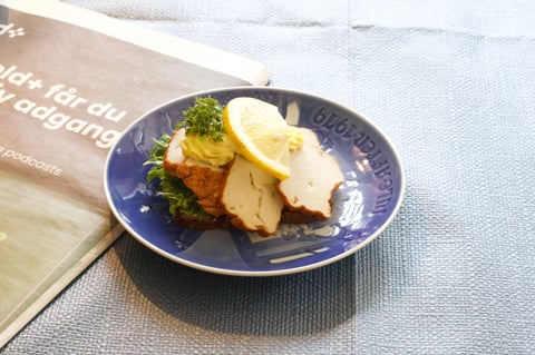 A blue plate with sliced fish, lemon wedges, and fresh broccoli on a light textured surface